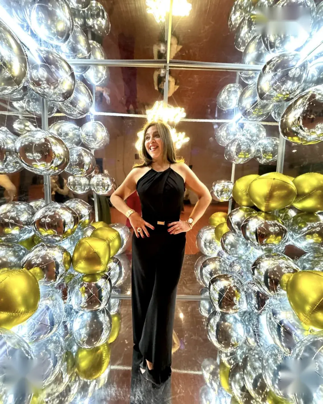 Cabina espejada rodeada de globos plateados y dorados en un salón