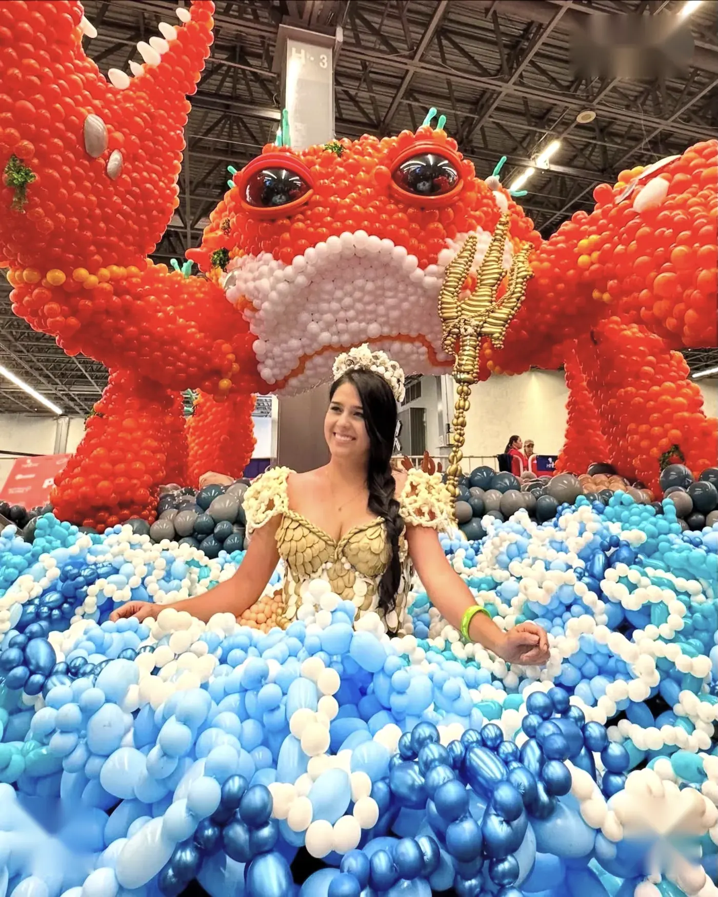 Escultura monumental de un dragón rojo hecho con globos, con una modelo vestida de sirena entre olas de globos azules