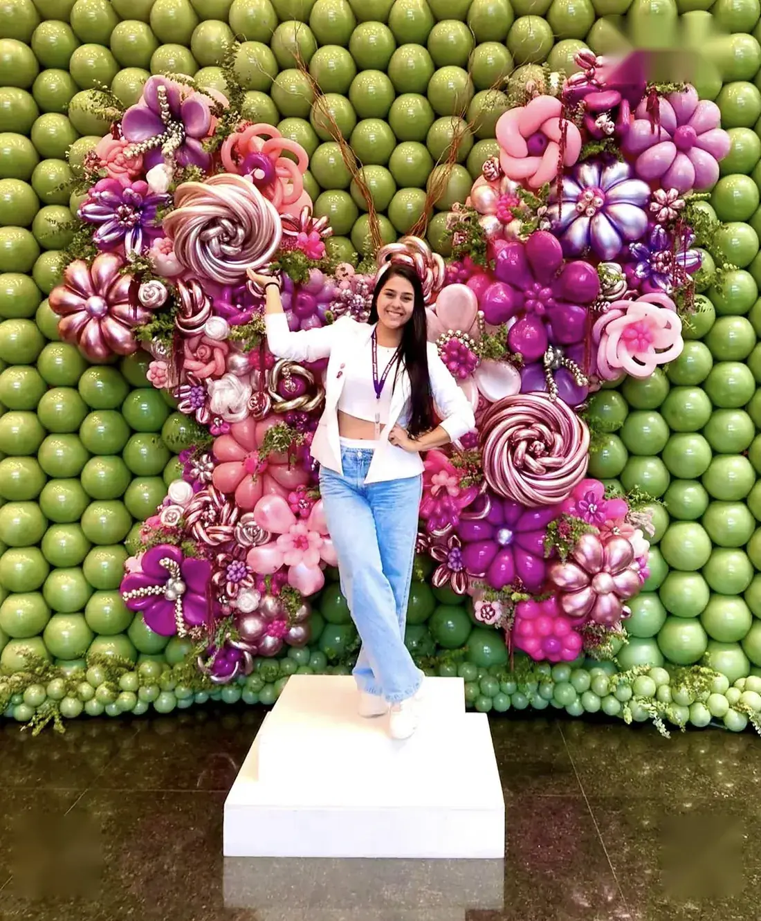 Muro de globos verdes con una mariposa gigante de globos rosas y morados
