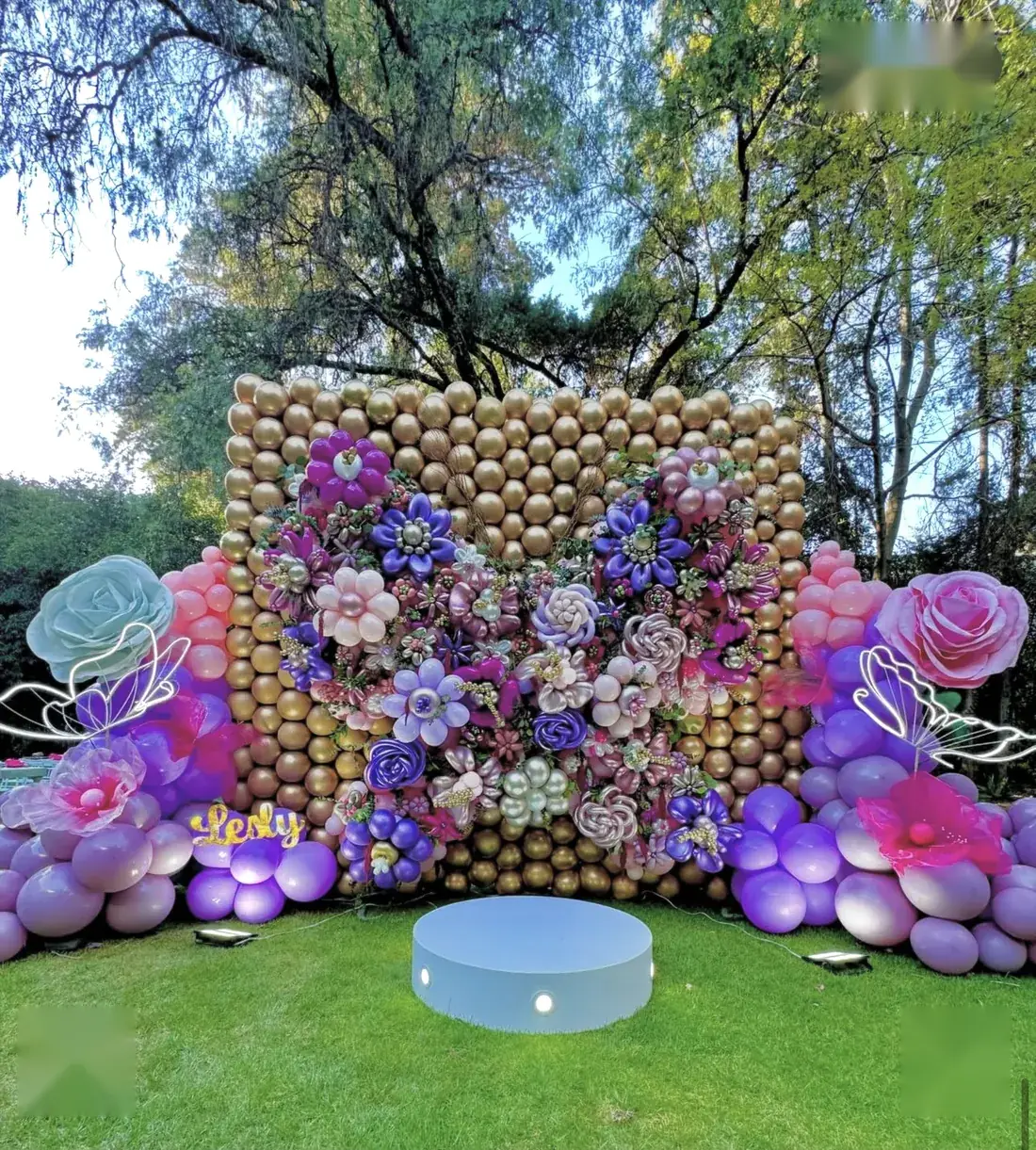 Muro de globos dorados con flores de globos y mariposas de neón en un jardín